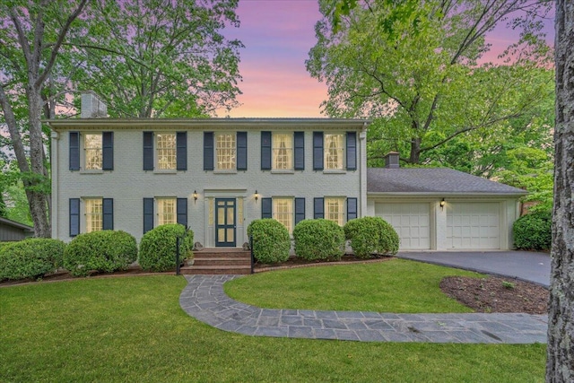 colonial inspired home with a yard, driveway, a chimney, and a garage