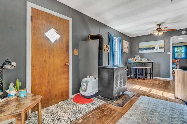 foyer featuring wood-type flooring, a wood stove, baseboards, and a ceiling fan