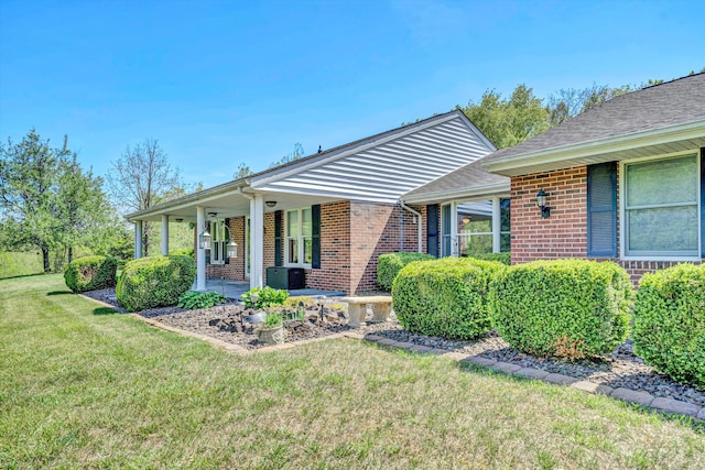 view of front of house featuring covered porch, brick siding, cooling unit, and a front yard