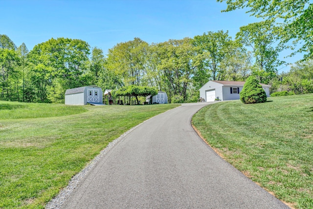 exterior space with an outdoor structure, aphalt driveway, a front yard, and a storage unit