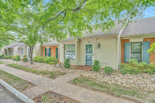 view of front of house featuring brick siding and roof with shingles