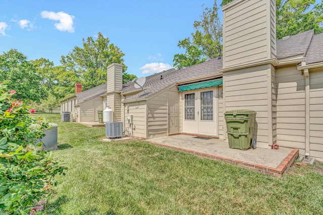 rear view of house featuring a yard, a shingled roof, a chimney, and central AC unit