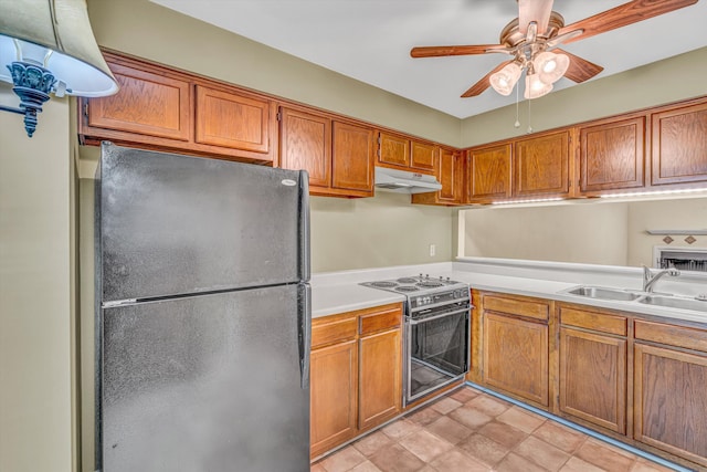 kitchen with a sink, light countertops, range with electric cooktop, freestanding refrigerator, and under cabinet range hood