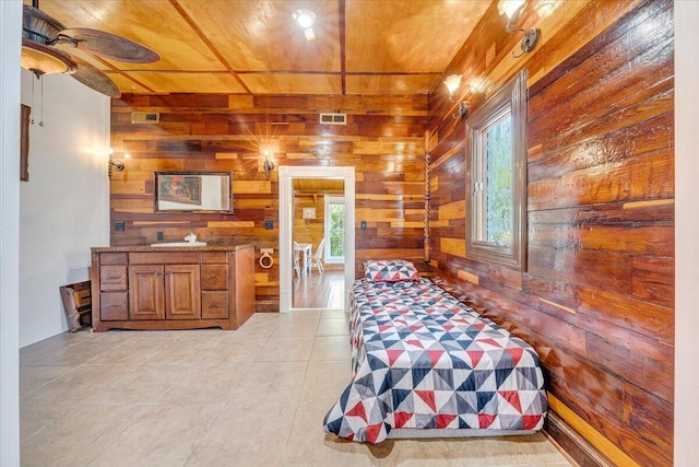bedroom with light tile patterned flooring, a sink, wood walls, wooden ceiling, and visible vents