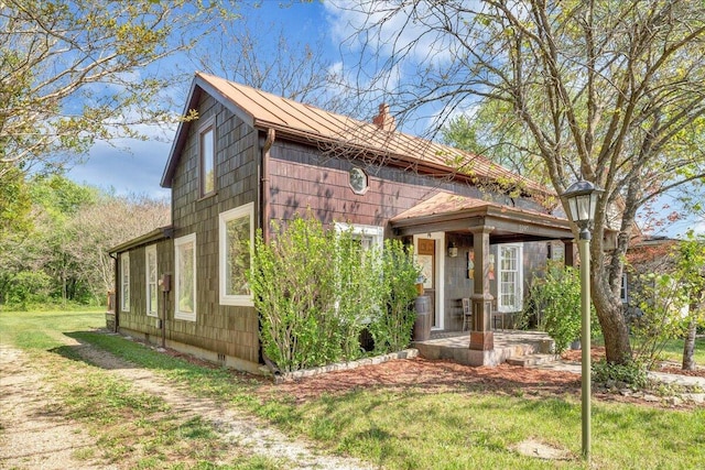 view of front of property with a front yard, metal roof, a chimney, and a standing seam roof