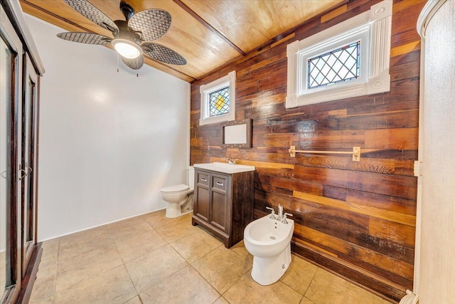 full bath featuring wooden walls, ceiling fan, tile patterned flooring, vanity, and toilet