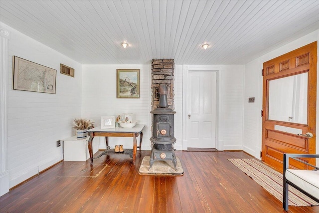 interior space featuring a wood stove, baseboards, wooden ceiling, visible vents, and hardwood / wood-style flooring