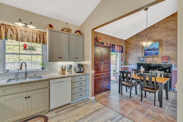 kitchen with white dishwasher, light stone countertops, hanging light fixtures, a sink, and vaulted ceiling