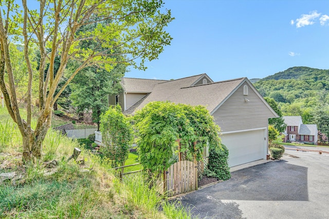 view of side of property with a garage, roof with shingles, and fence