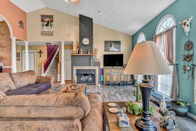 living room featuring arched walkways, a fireplace, wood finished floors, high vaulted ceiling, and ornate columns