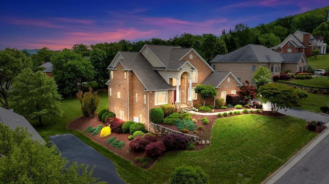 traditional-style house featuring an attached garage, brick siding, a yard, and driveway