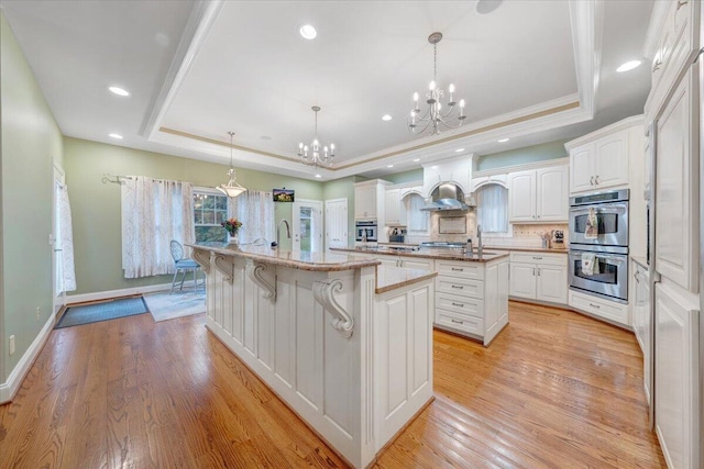 kitchen with double oven, a tray ceiling, a spacious island, a chandelier, and white cabinets