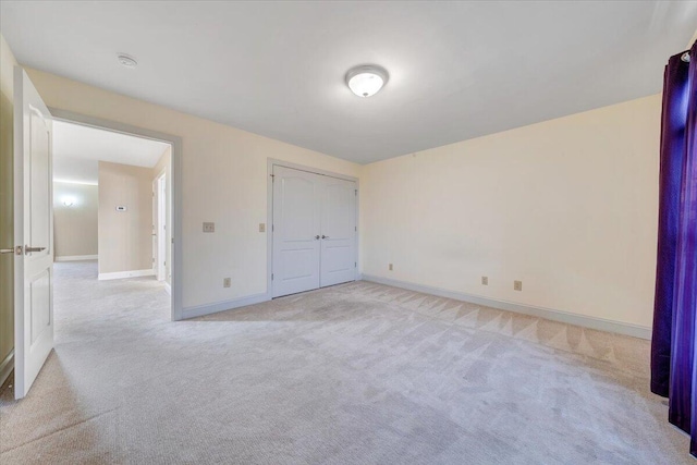 unfurnished bedroom with light carpet, baseboards, and a closet