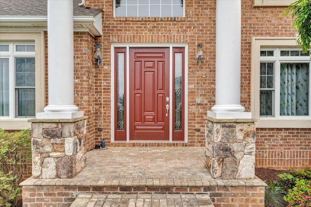 doorway to property featuring brick siding and a shingled roof