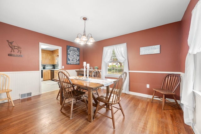 dining area with a chandelier, light wood-style flooring, visible vents, and a wainscoted wall