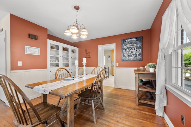 dining area with a chandelier, light wood-style flooring, and a wainscoted wall