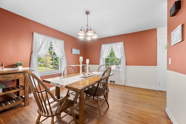 dining area with a notable chandelier, light wood-type flooring, and a wainscoted wall