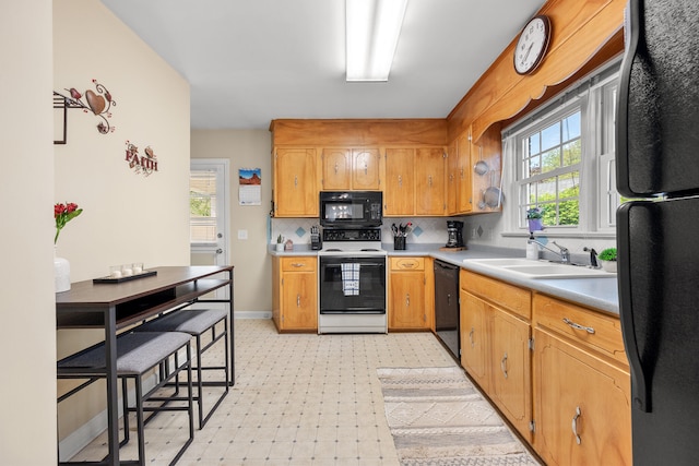 kitchen featuring baseboards, light floors, light countertops, a sink, and black appliances