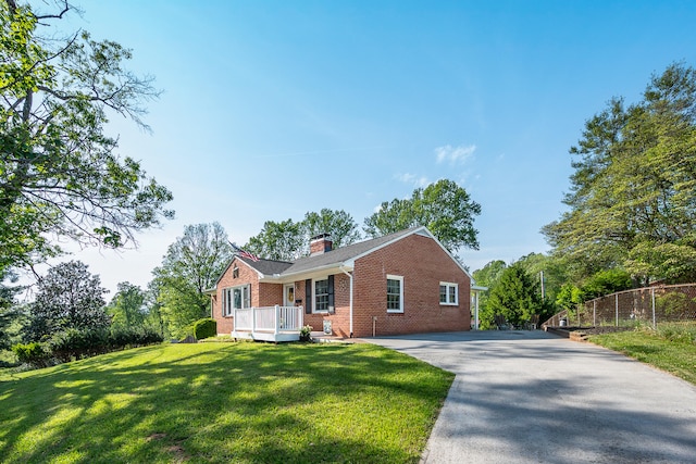 view of front of house with fence, a front lawn, brick siding, a chimney, and driveway