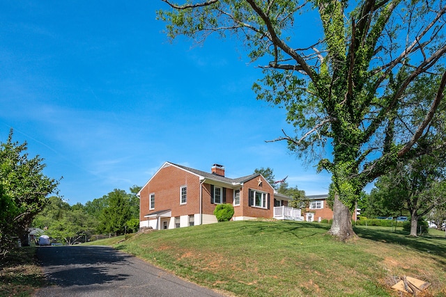 view of property exterior with driveway, a chimney, a lawn, brick siding, and an attached garage