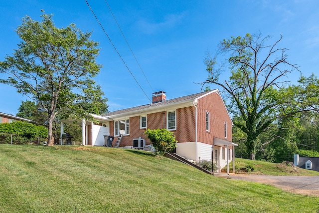 back of house featuring a chimney, a yard, central AC, and brick siding