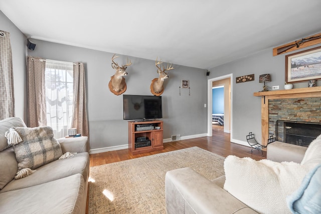living area featuring baseboards, visible vents, a stone fireplace, and wood finished floors