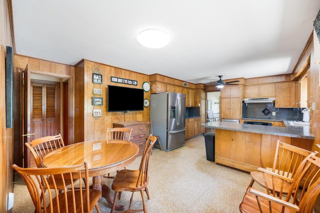 kitchen with a ceiling fan, a sink, a peninsula, wooden walls, and stainless steel fridge