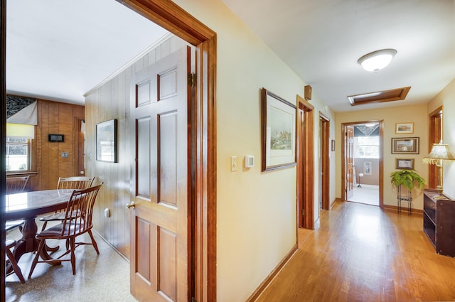 corridor featuring light wood-style floors, baseboards, and wooden walls