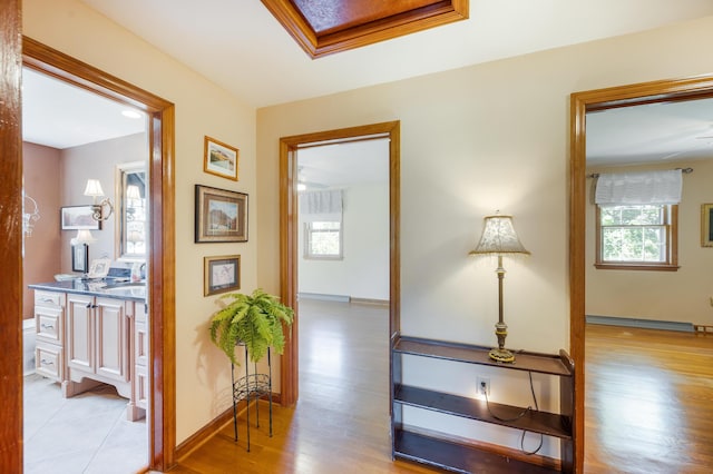 hallway with baseboard heating, baseboards, a healthy amount of sunlight, and light wood-style flooring