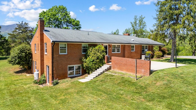 back of house featuring a lawn, a chimney, stairway, and brick siding