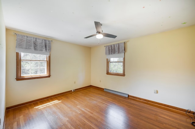 unfurnished room with a healthy amount of sunlight, baseboards, baseboard heating, and wood finished floors
