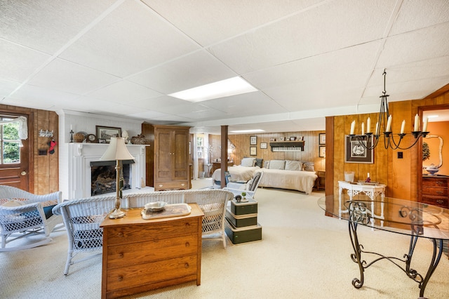 living area featuring wood walls, a fireplace with raised hearth, a drop ceiling, and carpet flooring