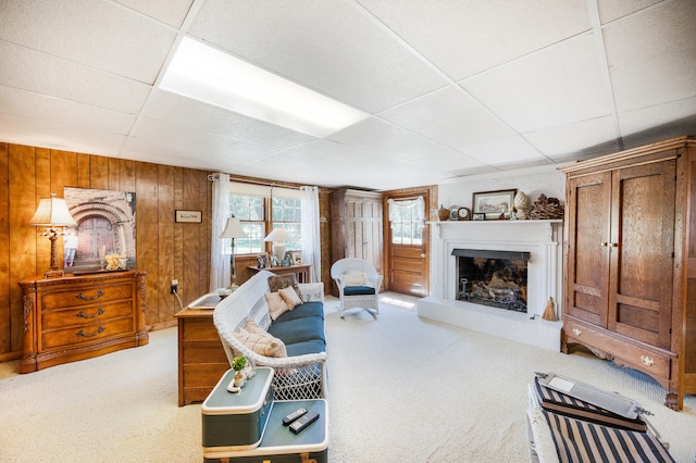 living room featuring carpet flooring, a fireplace with raised hearth, wood walls, and a paneled ceiling