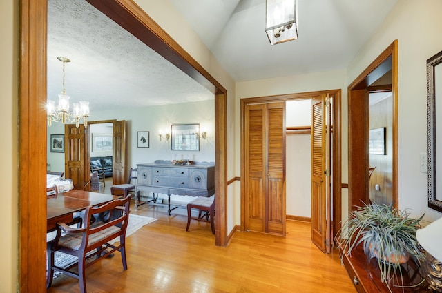 hallway featuring baseboards, a chandelier, plenty of natural light, and light wood finished floors