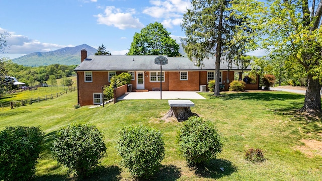 rear view of property featuring fence, a patio, a chimney, brick siding, and a yard