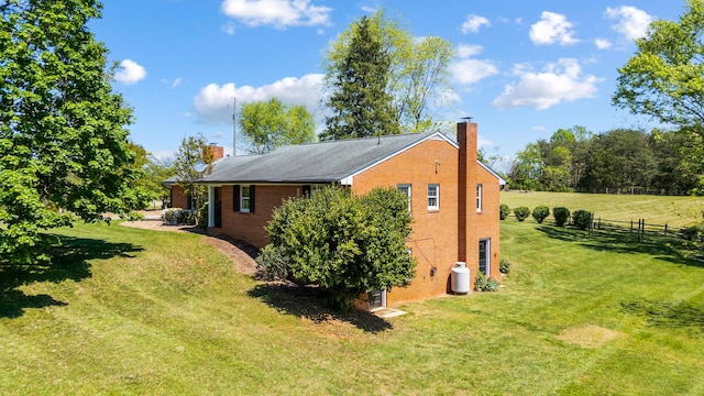 view of home's exterior with a lawn, fence, a chimney, and brick siding