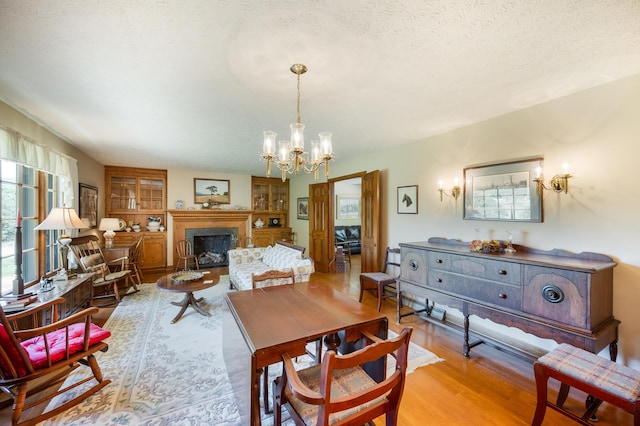 dining space with a textured ceiling, wood finished floors, a chandelier, and a fireplace