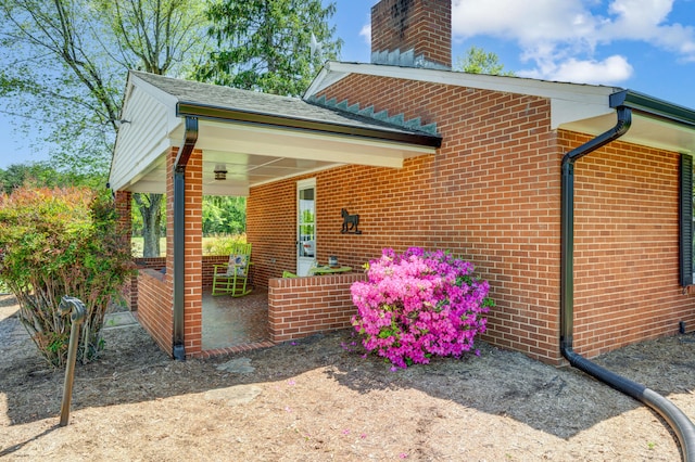 view of home's exterior with covered porch, a chimney, and brick siding