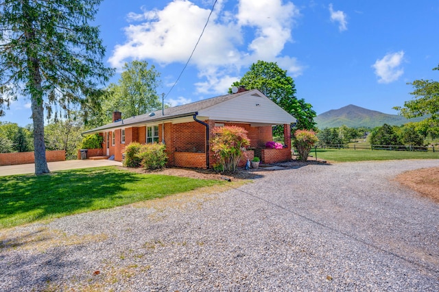 view of front facade featuring fence, brick siding, a front yard, a mountain view, and a chimney