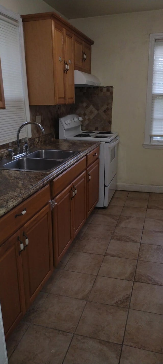 kitchen with light tile patterned flooring, a sink, brown cabinetry, range hood, and white electric range