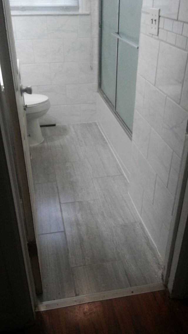 bathroom featuring combined bath / shower with glass door, toilet, and wood finished floors