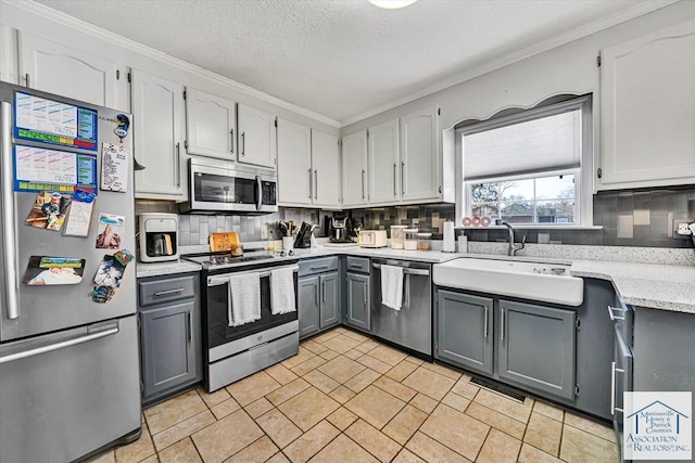 kitchen with crown molding, a sink, appliances with stainless steel finishes, backsplash, and gray cabinetry