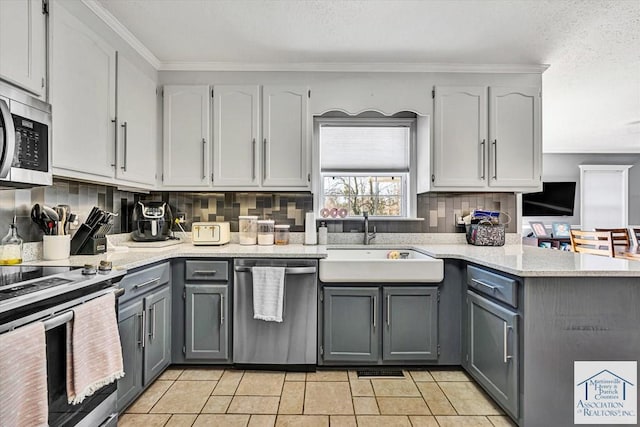 kitchen with a peninsula, a sink, backsplash, gray cabinetry, and stainless steel appliances