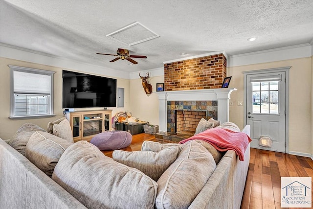living area with a tiled fireplace, a textured ceiling, crown molding, and hardwood / wood-style floors