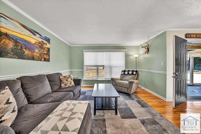 living area featuring baseboards, a textured ceiling, ornamental molding, and wood finished floors
