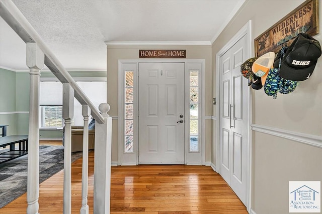 foyer entrance featuring light wood-type flooring, ornamental molding, baseboards, and stairway