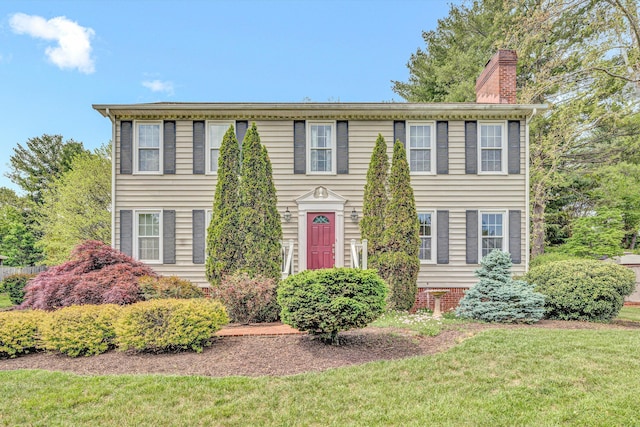 colonial inspired home with a chimney and a front lawn