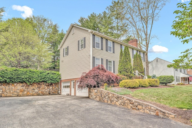view of side of home featuring a chimney, driveway, an attached garage, and a yard