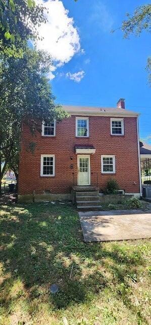 view of front of home with brick siding, a chimney, and entry steps