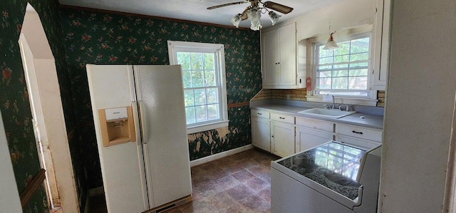 kitchen with baseboards, stove, wallpapered walls, a sink, and white fridge with ice dispenser